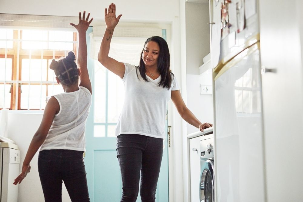 Mother and child smiling and giving each other a high five in a bright kitchen, celebrating a small accomplishment.