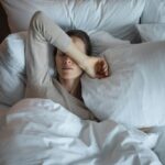 Eagle View - Bed Rotting and Other Hidden Signs of Depression. A young woman lays in bed upset. She covers her face with her farm as she rests on a pillow with the covers pulled up.