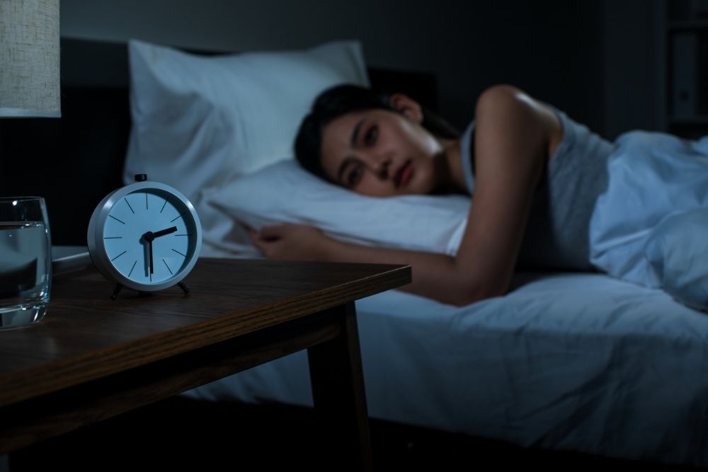 Eagle View - Sleep Deprivation and Emotional Regulation. A woman lies in bed awake staring at a clock. It is the middle of the night.