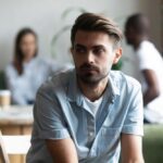 Eagle View - Why Neurodivergent Individuals Often Struggle With Mental Health Challenges - Edited. A man sits looking upset and dejected as friends in the foreground talk amongst themselves about