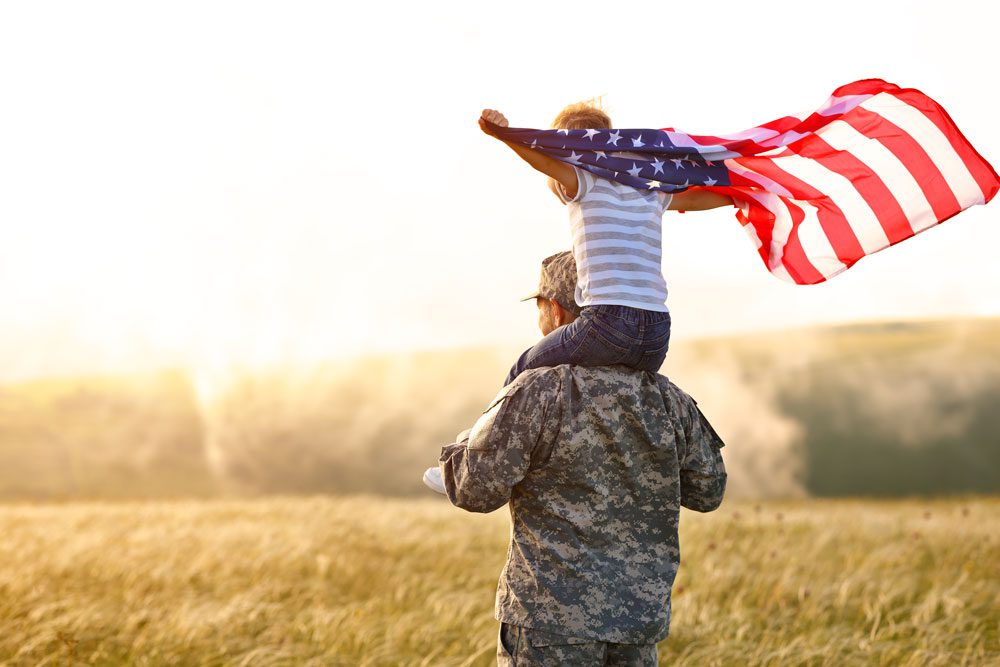 First Responder or Veteran with child on shoulders who is holding an American flag